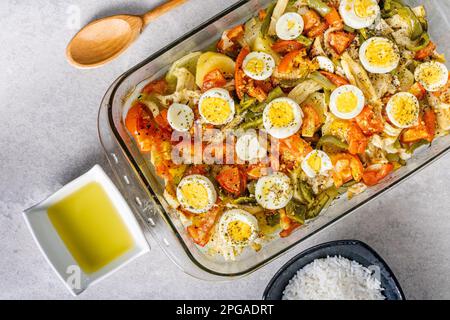 Gomes de sa morue rôtie dans de l'huile d'olive avec tomates, poivrons, oignons, œufs durs et origan. Dans un plat rectangulaire en verre. Détail bois sp Banque D'Images