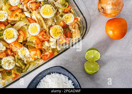 Gomes de sa morue rôtie dans de l'huile d'olive avec tomates, poivrons, oignons, œufs durs et origan. Dans un plat rectangulaire en verre. Détail bois sp Banque D'Images