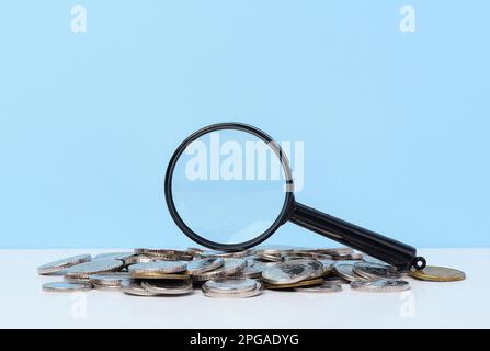 Une pile de pièces de monnaie en métal et une loupe en plastique sur fond bleu. Le concept de l'augmentation des impôts, des subventions Banque D'Images