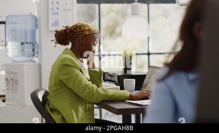 Adulte afro-américain souffrant de migraine à son bureau, travaillant sous pression avec un rapport annuel. Femme entrepreneur se sentant malade et malheureux avec mal de tête douloureux, étant en tension pour augmenter le profit. Banque D'Images