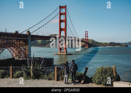 Un couple prend une photo avec le Golden Gate Bridge en arrière-plan. Le couple tient les mains et regarde l'un l'autre, avec le pont fournissant une belle et romantique toile de fond à leur photo. Le célèbre Golden Gate Bridge, l'un des monuments les plus reconnaissables des États-Unis. Le pont, qui traverse le détroit du Golden Gate et relie San Francisco au comté de Marin, est une merveille d'ingénierie depuis son achèvement en 1937. Le Golden Gate Bridge est devenu un symbole de San Francisco et une destination touristique populaire, attirant des millions de visiteurs chaque année. Le pont ne l'est pas Banque D'Images