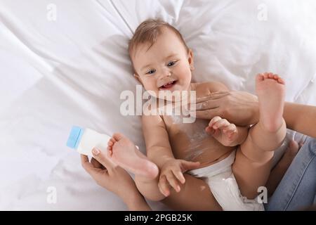 Mère appliquant de la poudre à dépoussiérer sur son bébé sur le lit, vue de dessus Banque D'Images