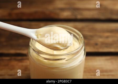 Délicieuse mayonnaise et cuillère dans un pot en verre sur une table en bois, en gros plan Banque D'Images