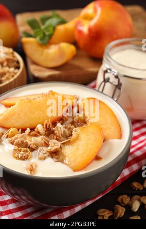 Savoureux yaourt à la pêche avec granola et morceaux de fruits dans un bol sur la table Banque D'Images