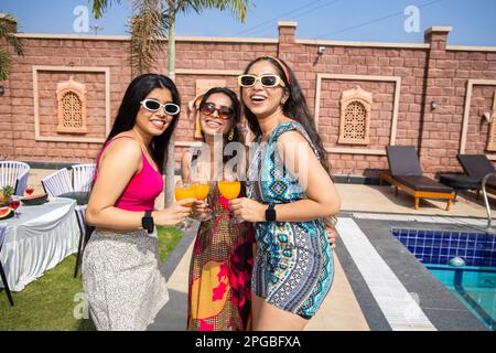 Trois belles jeunes filles indiennes portant des lunettes de soleil s'amuser ensemble en tenant des verres de cocktail pendant la chaude journée d'été à l'hôtel. Conce d'été Banque D'Images