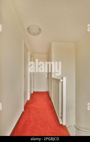 un long couloir avec moquette rouge et murs blancs dans un immeuble d'appartements, pris de la porte d'entrée à gauche Banque D'Images