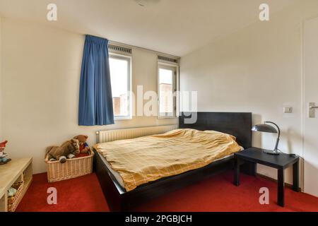 une chambre avec un lit, un bureau et une fenêtre dans le sol arrière est un tapis orange sur la moquette rouge Banque D'Images