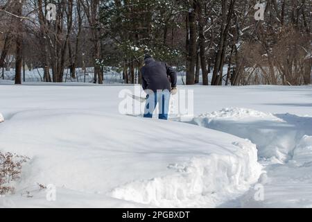 Vue sur le paysage d'un adulte méconnaissable qui pelait de la neige profonde sur une terrasse résidentielle par une belle journée d'hiver Banque D'Images
