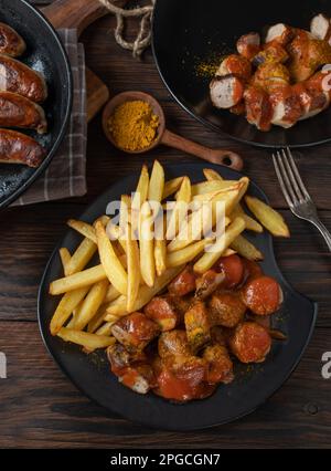 Saucisse de Currywurst ou curry avec frites sur fond rustique et en bois. Repas rapide allemand traditionnel Banque D'Images