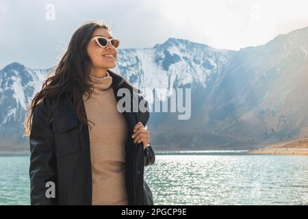Jeune femme positive se tenant près du lac en arrière-plan des montagnes Banque D'Images