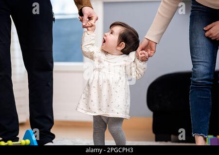 Rognez les parents méconnaissables tenant les mains d'une petite fille mignonne dans des vêtements décontractés qui marchent ensemble dans l'appartement Banque D'Images