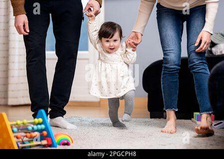 Rognez les parents méconnaissables tenant les mains d'une petite fille mignonne dans des vêtements décontractés qui marchent ensemble dans l'appartement Banque D'Images