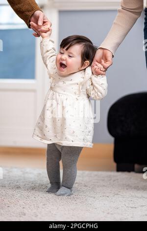 Rognez les parents méconnaissables tenant les mains d'une petite fille mignonne dans des vêtements décontractés qui marchent ensemble dans l'appartement Banque D'Images