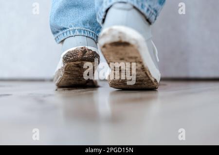 Un enfant méconnaissable marchant à l'intérieur de l'appartement dans des baskets sales et laissant des taches dans le sol. Banque D'Images