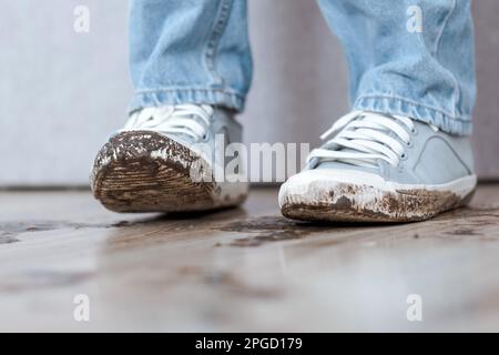 Une personne méconnaissable dans un Jean bleu et des chaussures blanches sales dans l'appartement. Présence de boue à l'intérieur sur le sol. Banque D'Images