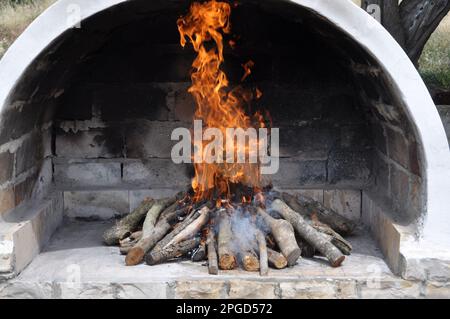 Cheminée de jardin avec une cheminée, faite de vieilles briques, avec un feu à l'intérieur.four extérieur en brique blanche avec un seau en bois Banque D'Images