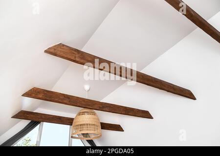 Poutres décoratives en bois marron dans la salle de séjour de la maison plafond de couleur blanche. Jolie décoration moderne et contrastée. Banque D'Images