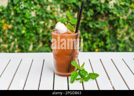 Thé vert glacé avec litchi et menthe sur table en bois blanc contre feuilles vertes avec espace de copie Banque D'Images