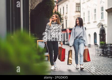 Deux jeunes femmes qui font du shopping dans le centre-ville, se promenant avec des sacs de papier dans leurs mains Banque D'Images