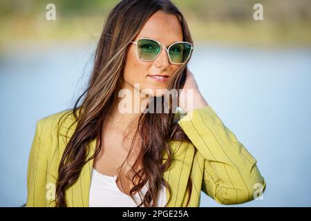 Jeune modèle féminin en mode rétro posé dans des lunettes de soleil teintées vertes Banque D'Images