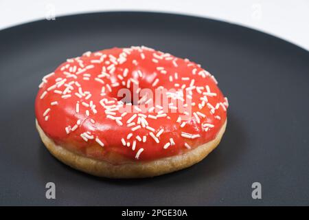 Grand donut à la glaçure rouge et parsemé sur un fond noir Banque D'Images