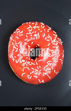 Grand donut à la glaçure rouge et parsemé sur un fond noir Banque D'Images
