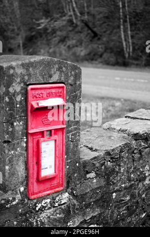 Une boîte aux lettres rouge est posée sur un mur de briques dans un environnement suburbain, avec une route visible en arrière-plan Banque D'Images