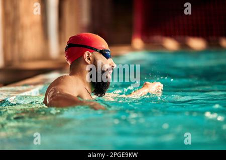 Un jeune homme nage dans la piscine avec une casquette rouge et des lunettes de natation, s'entraîner dans la piscine, se préparer à la compétition, nager, ramper à l'avant, bre Banque D'Images