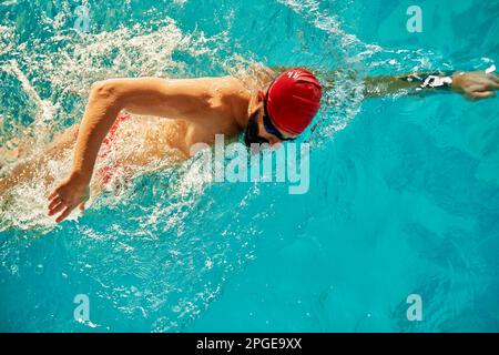 Un jeune homme nage dans la piscine avec une casquette rouge et des lunettes de natation, s'entraîner dans la piscine, se préparer à la compétition, nager, ramper à l'avant, bre Banque D'Images