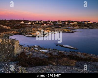 Le ciel du soir est peint en orange et en rouge, se reflétant au large de la mer calme. Les maisons perchées sur la côte donnent la place à un paysage suédois époustouflant. Banque D'Images