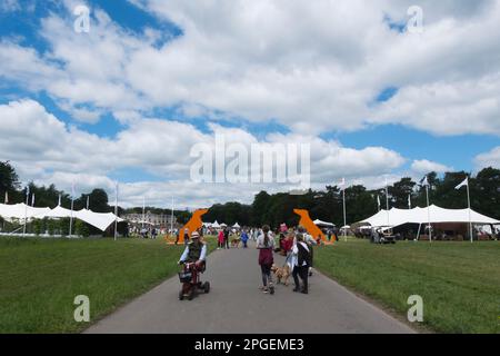 Les gens qui marchent devant deux énormes silhouettes en bois orange de Hounds à l'entrée de Goodwoof, les Kennels, Goodwood, West Sussex, Royaume-Uni Banque D'Images