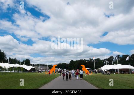 Les gens qui marchent devant deux énormes silhouettes en bois orange de Hounds à l'entrée de Goodwoof, les Kennels, Goodwood, West Sussex, Royaume-Uni Banque D'Images