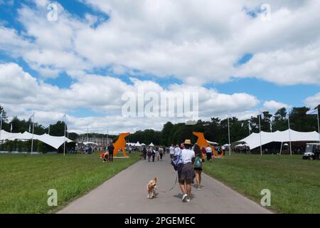 Les gens qui marchent devant deux énormes silhouettes en bois orange de Hounds à l'entrée de Goodwoof, les Kennels, Goodwood, West Sussex, Royaume-Uni Banque D'Images