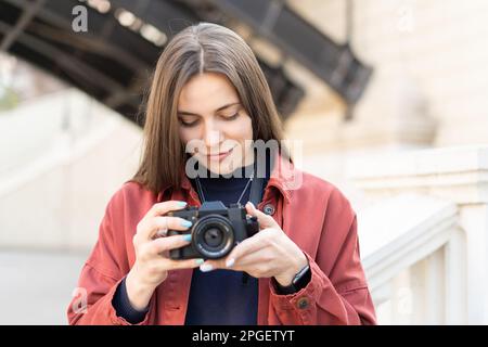 Gros plan d'une charmante brunet qui vérifie sa photo sur l'appareil photo qui se trouve à l'extérieur dans une rue moderne Banque D'Images