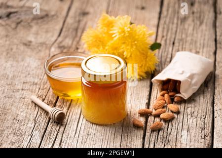 Miel dans un pot en verre fermé et un bol sur fond de bois. Composition de bocaux à miel, de louche, de noix dans un sac et de fleurs jaunes. Des aliments sains. Banque D'Images