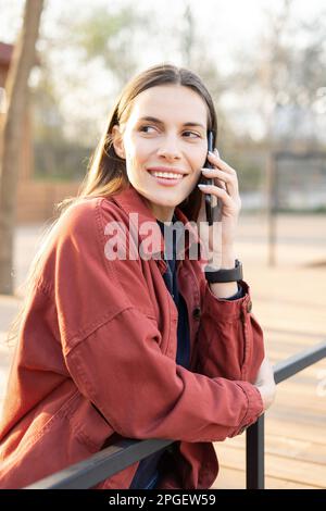 Une femme animée d'âge moyen parle sur son téléphone mobile avec un sourire éclatant à l'extérieur des voies latérales Banque D'Images