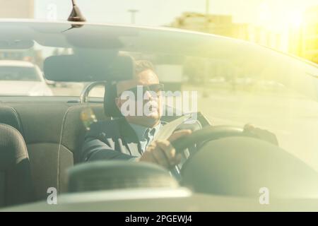 un jeune homme d'affaires roule dans une voiture convertible en été avec une expression satisfaite sur son visage. Banque D'Images
