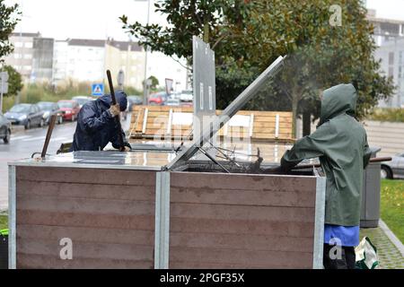 Un travailleur gère une affiche communautaire sous la pluie. La composter est placée dans une zone résidentielle commune pour recycler et réduire la wast biologique Banque D'Images