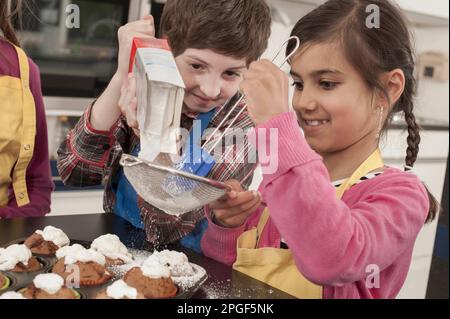 Les étudiants saupoudrent du sucre en poudre sur les muffins de la classe d'économie domestique, Bavière, Allemagne Banque D'Images