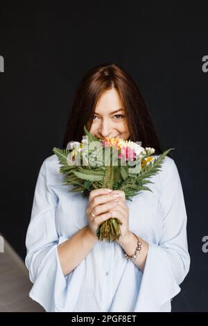 femme enceinte heureuse dans une chemise bleue tenant un bouquet de fleurs Banque D'Images