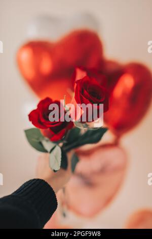 Personne tenant des roses rouges près des ballons d'hélium de coeur Banque D'Images