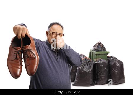 Homme mature tenant une paire de chaussures ratées près d'une poubelle isolée sur fond blanc Banque D'Images