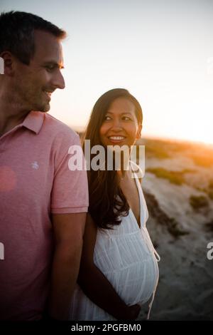 Femme enceinte souriant au mari sur la plage à San Diego au coucher du soleil Banque D'Images