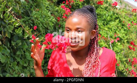 Femme africaine noire sentant des fleurs et souriant Banque D'Images