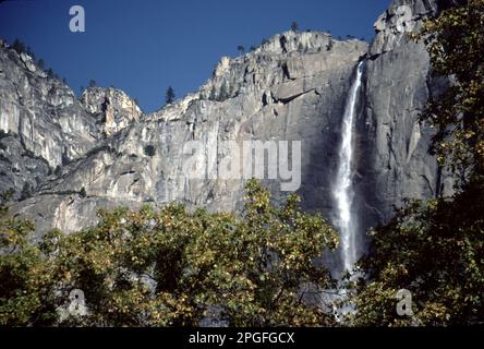 Parc national de Yosemite. ENV. ÉTATS-UNIS 1984. Yosemite Upper, Middle et Lower Falls. Repérez le cône de glace à la base de l'automne supérieur pendant l'hiver et le ruissellement torant d'avril à juin. Les chutes de Yosemite, l'une des plus hautes du monde, sont en fait composées de trois chutes distinctes : la chute de Yosemite supérieure (1 430 pieds), les cascades moyennes (675 pieds) et la chute de Yosemite inférieure (320 pieds). La meilleure observation des chutes de Yosemite est la région autour de Sentinel Meadow et de la Yosemite Chapel. Nevada Falls, Bridalveil Falls et Vernal Falls vus depuis le fond de la vallée de Yosemite. Banque D'Images