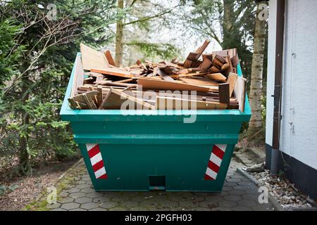 contenant vert rempli de bois, à côté d'une maison Banque D'Images