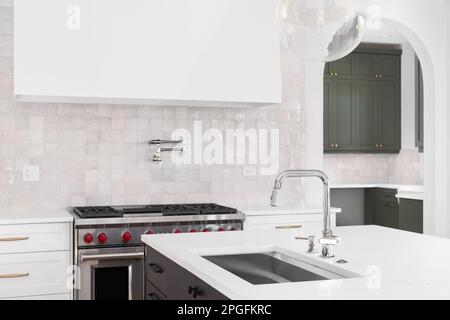Un détail de cuisine avec un évier sur le comptoir en marbre d'une île avec une cuisinière, une hotte, et une dosseret de carrelage en arrière-plan. Banque D'Images