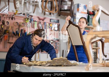 Artisans professionnels restaurateurs en uniforme rénovation chaise ancienne cadre de miroir tout en travaillant dans un atelier de réparation Banque D'Images