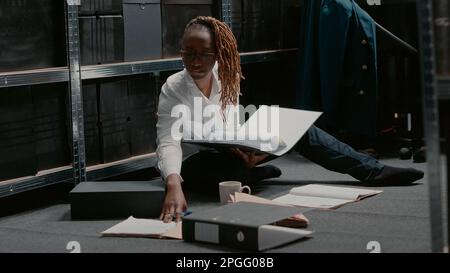 Un agent de droit ciblé examine les dossiers dans un dossier, lisant des indices criminels importants dans les archives de la police. Une femme inspectrice fait des recherches pour trouver un suspect avec des photos de surveillance. Prise de vue à main levée. Banque D'Images