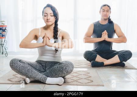 Deux personnes d'âge moyen font du yoga à l'intérieur, avec beaucoup de lumière du soleil entrant par la fenêtre, faisant des positions profondes de méditation. Il y en a beaucoup Banque D'Images